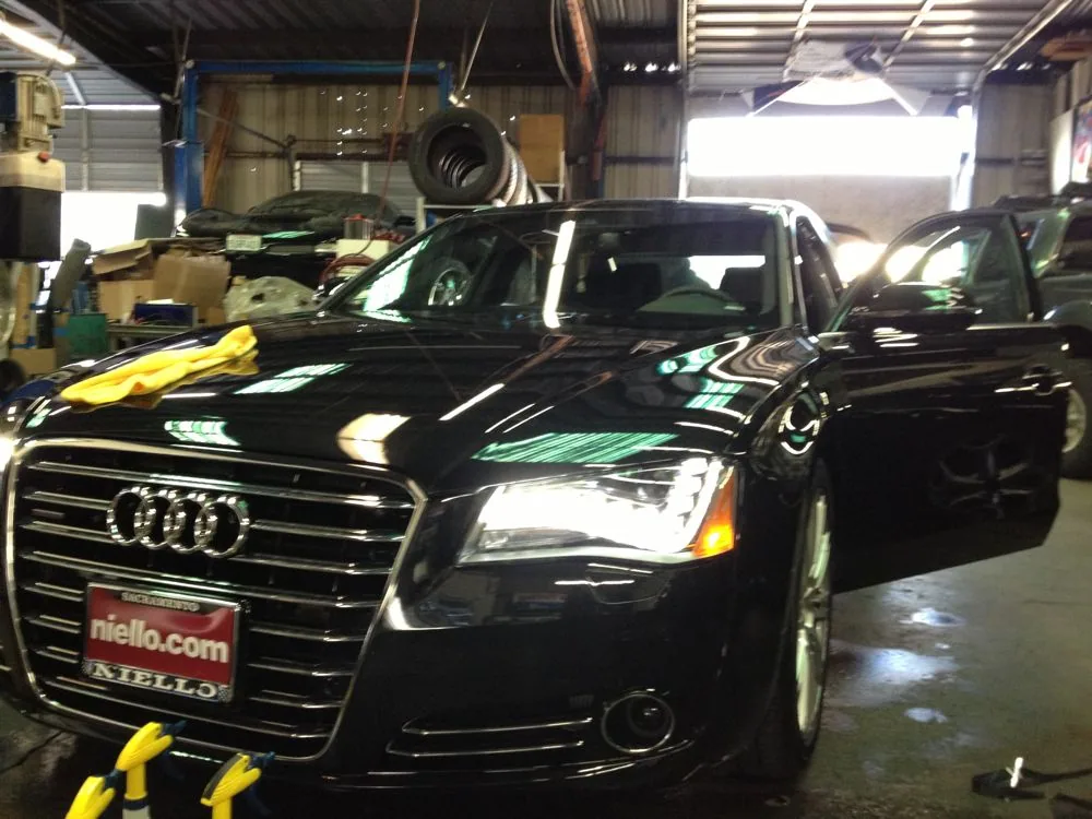 Black Audi sedan in garage with open door, yellow towing straps attached, other vehicles visible in background