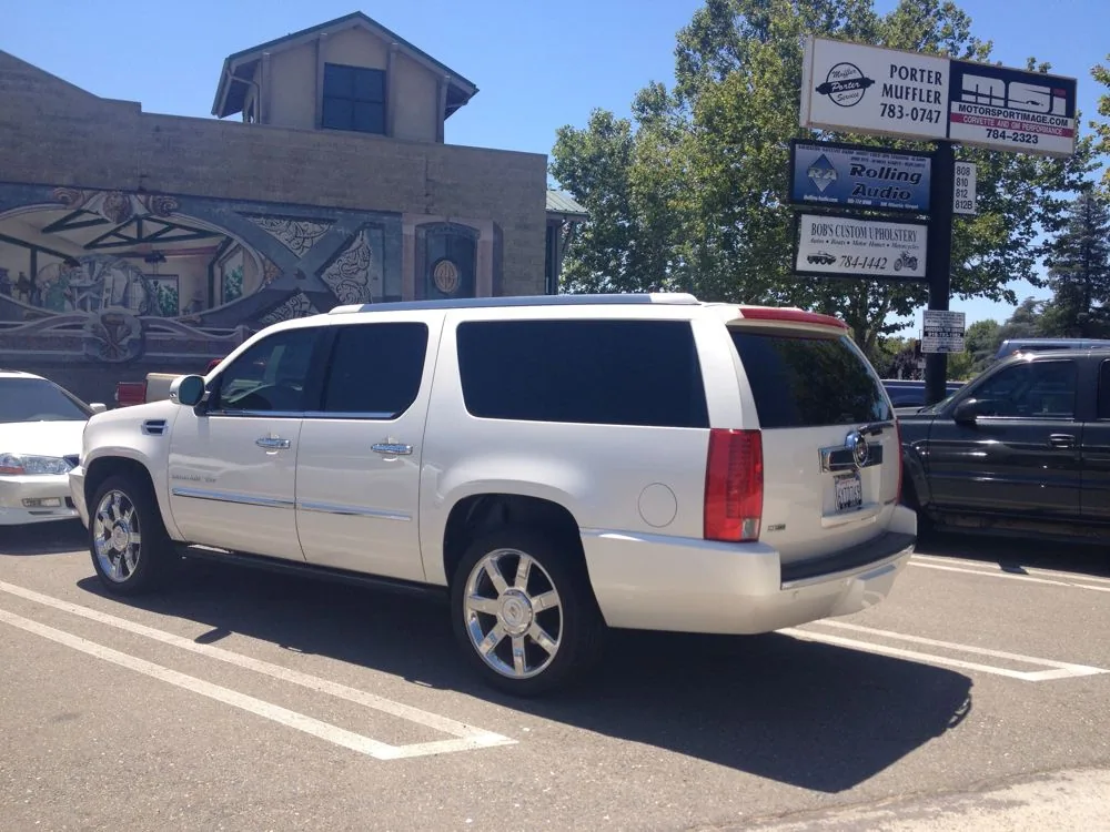 White Cadillac Escalade parked in lot with business signage and mural building visible