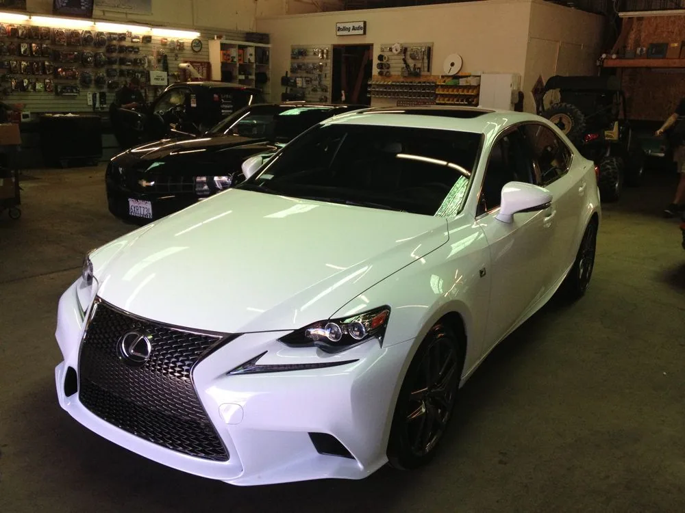 White luxury sedan with dark windows parked in automotive workshop with tools and equipment visible in background