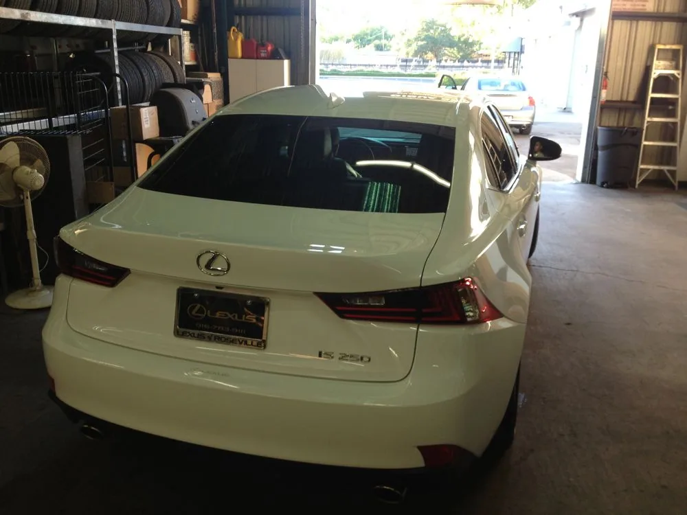 White Lexus IS sedan parked in automotive garage with tinted windows and equipment storage
