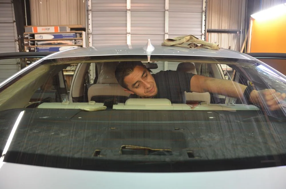 Person installing window tint on a car's windshield in an automotive shop