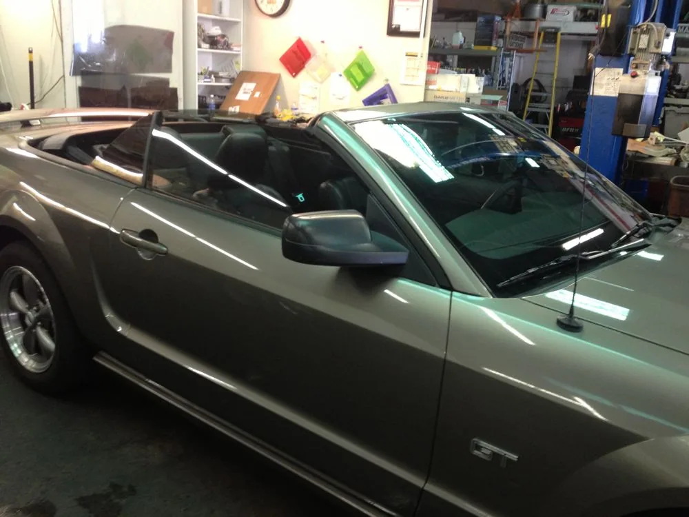 Silver convertible with retracted roof in indoor shop space with shelving and tinted window samples on walls