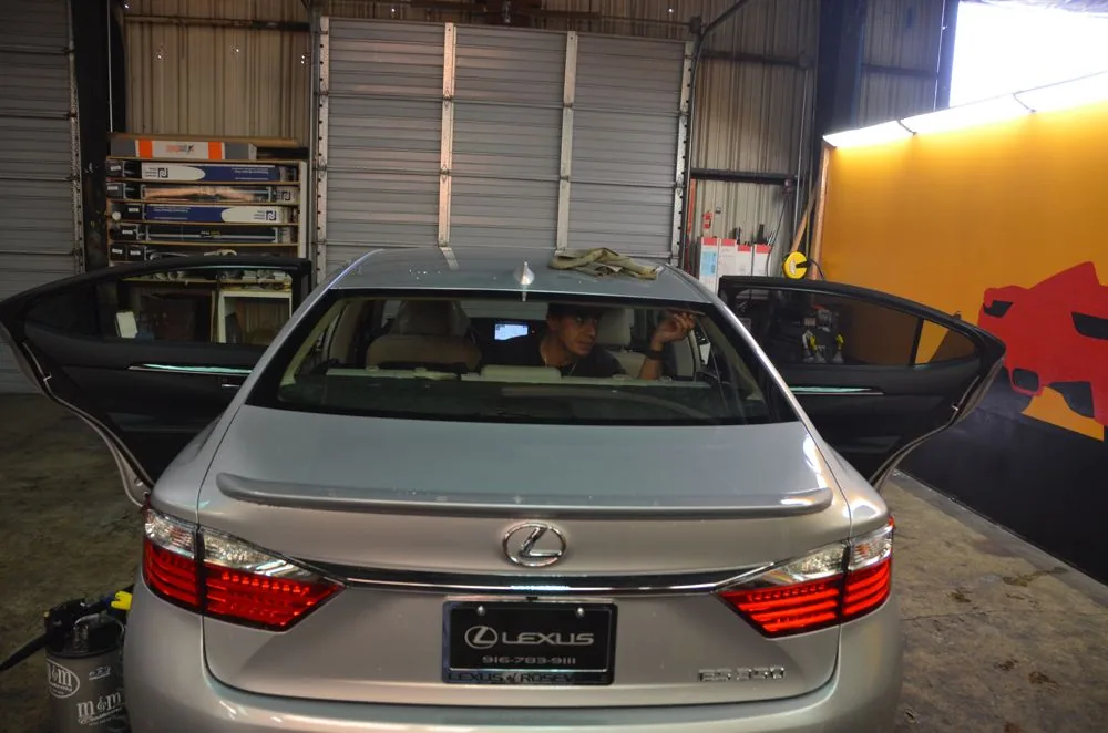Silver Lexus sedan with open doors in automotive workshop showing tinted windows installation