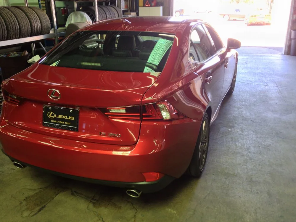 Red sedan parked in automotive service garage with tires and equipment visible in background