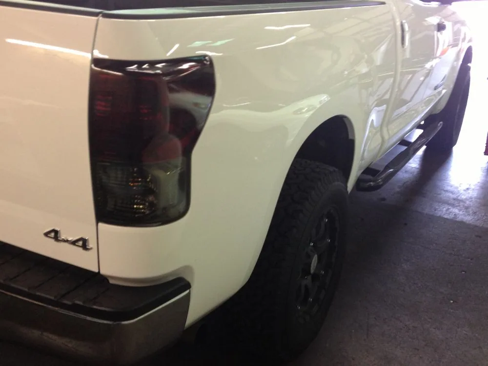 White pickup truck rear quarter view showing tinted tail light and black wheel in parking area