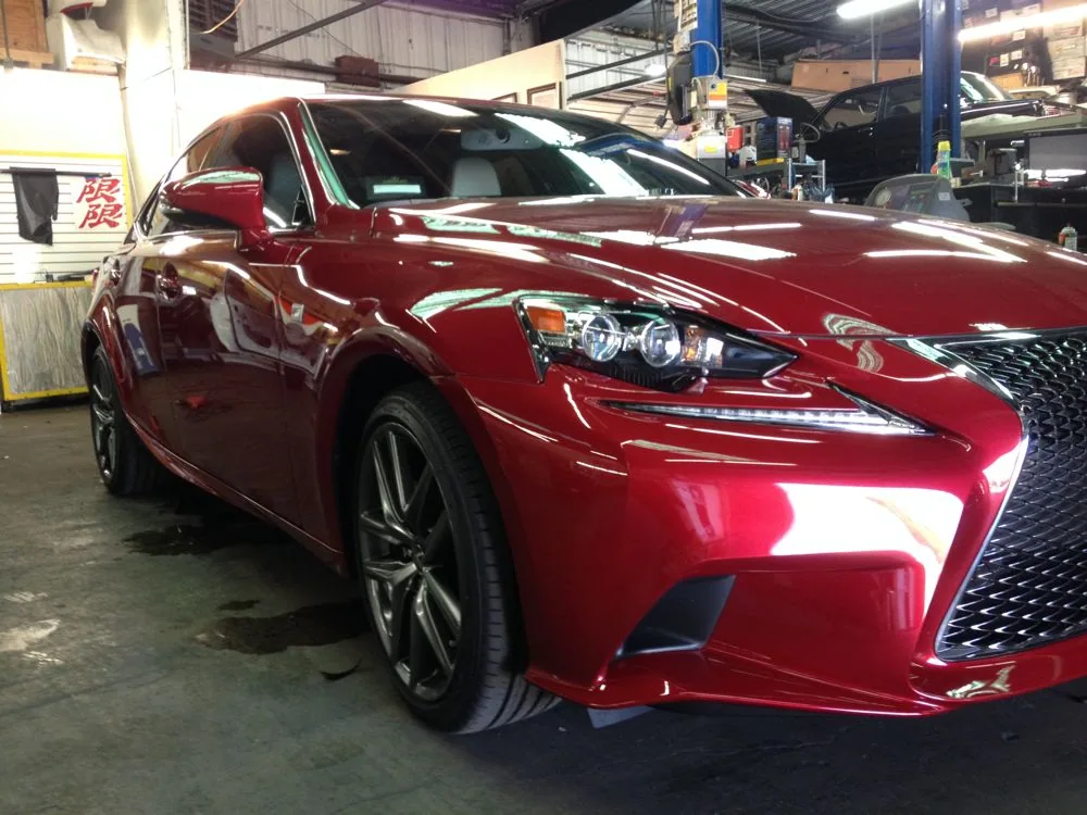 Red luxury sedan parked in auto service facility with industrial ceiling and equipment visible