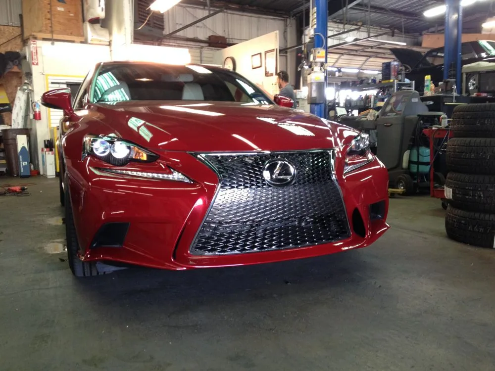 Red Lexus sedan in automotive service garage with blue lift and tools visible