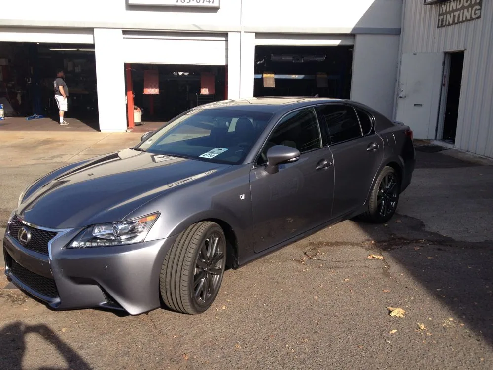 Silver Lexus sedan with racing stripes parked in front of a commercial garage with white frame and red doors