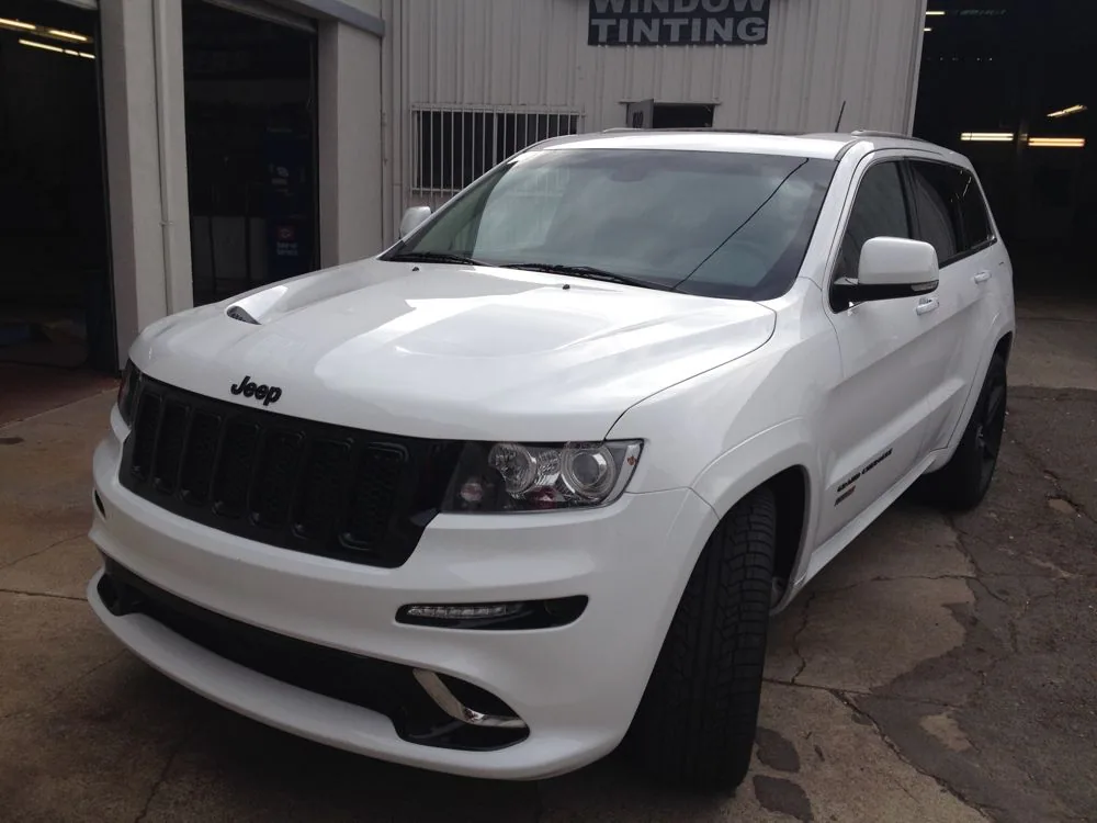 White Jeep Grand Cherokee parked outside a window tinting shop with dark tinted windows and white-painted mirror covers