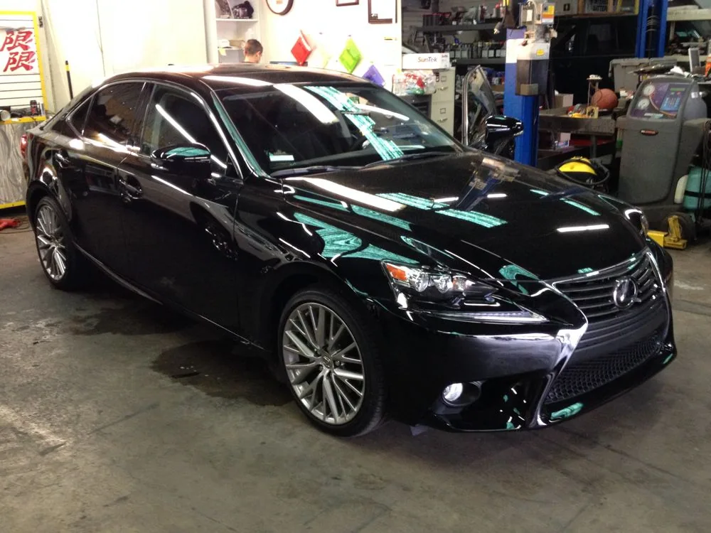 Black luxury sedan parked in automotive workshop with tools and equipment visible in background