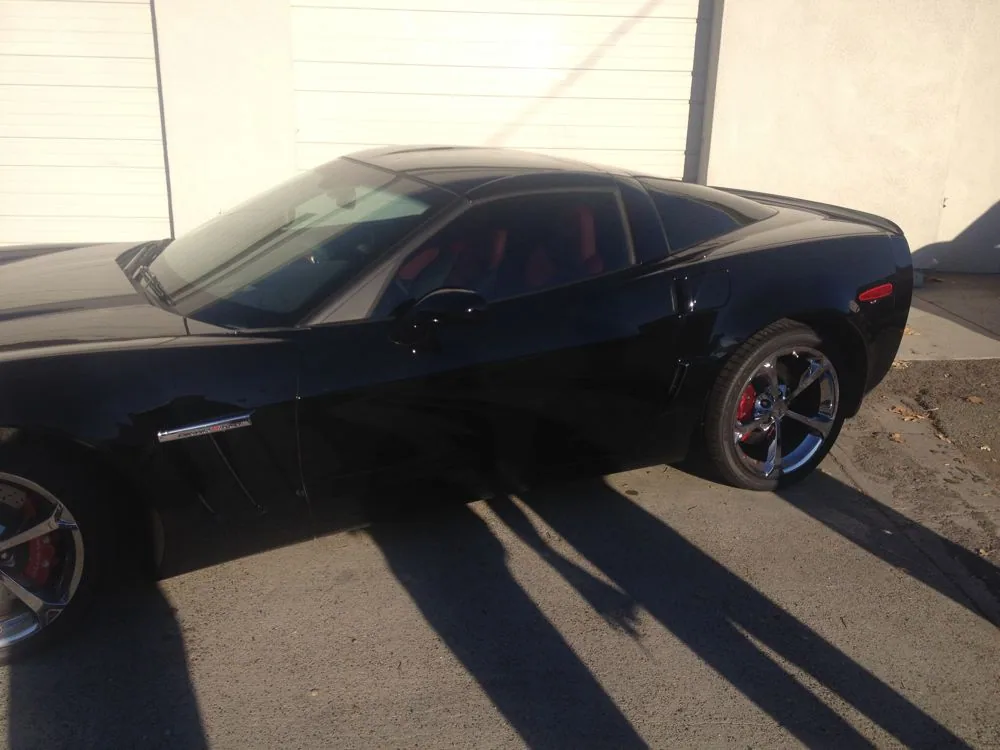 Black sports car with red interior and chrome wheels parked in garage with natural sunlight casting shadows