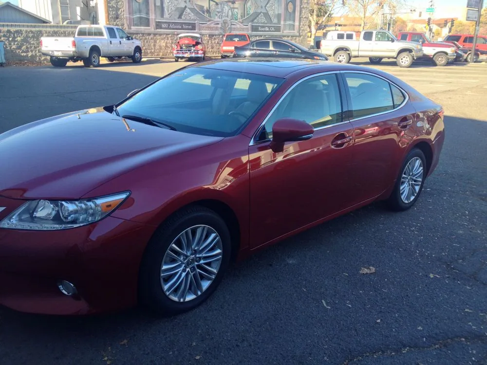 Burgundy sedan with alloy wheels parked in lot with other vehicles and buildings in background