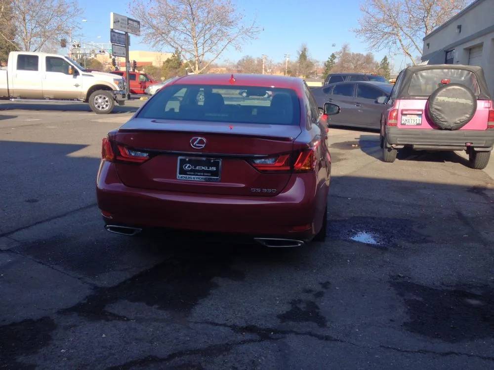 Burgundy Lexus sedan parked in dealership lot with other vehicles and bare trees in background