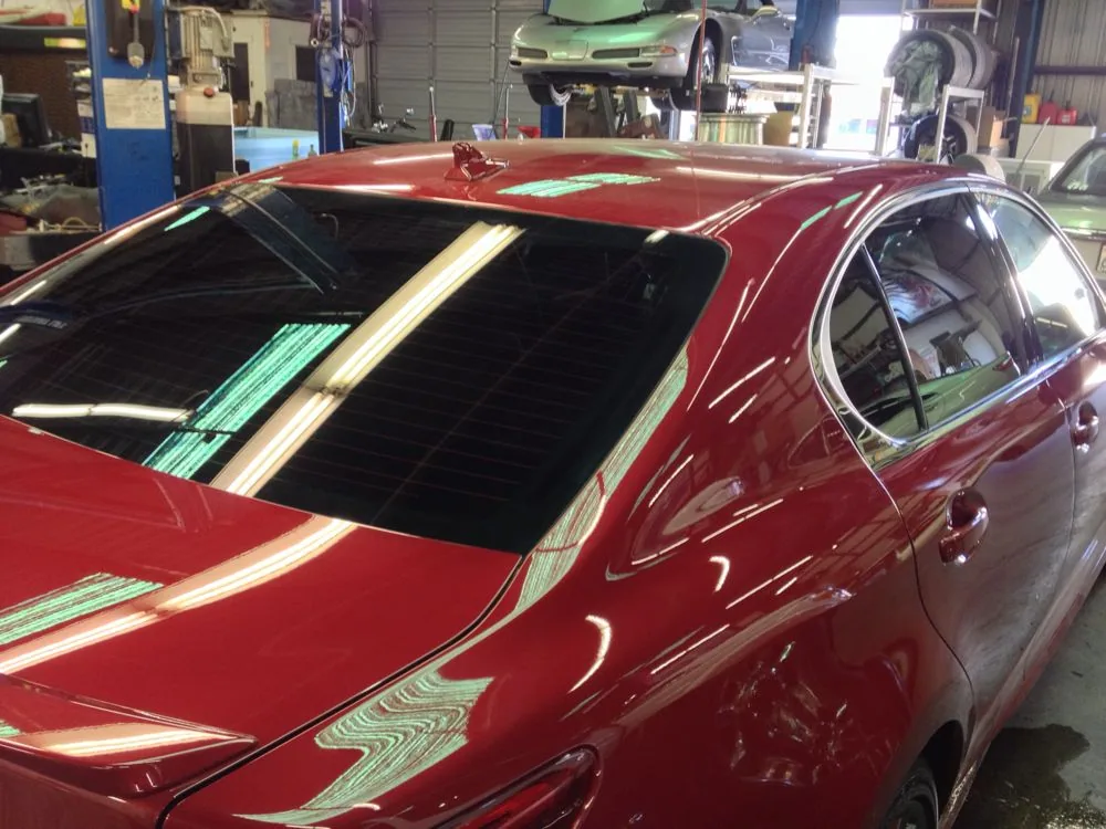 Red classic car with open hood in automotive service garage with lift and other vehicles visible