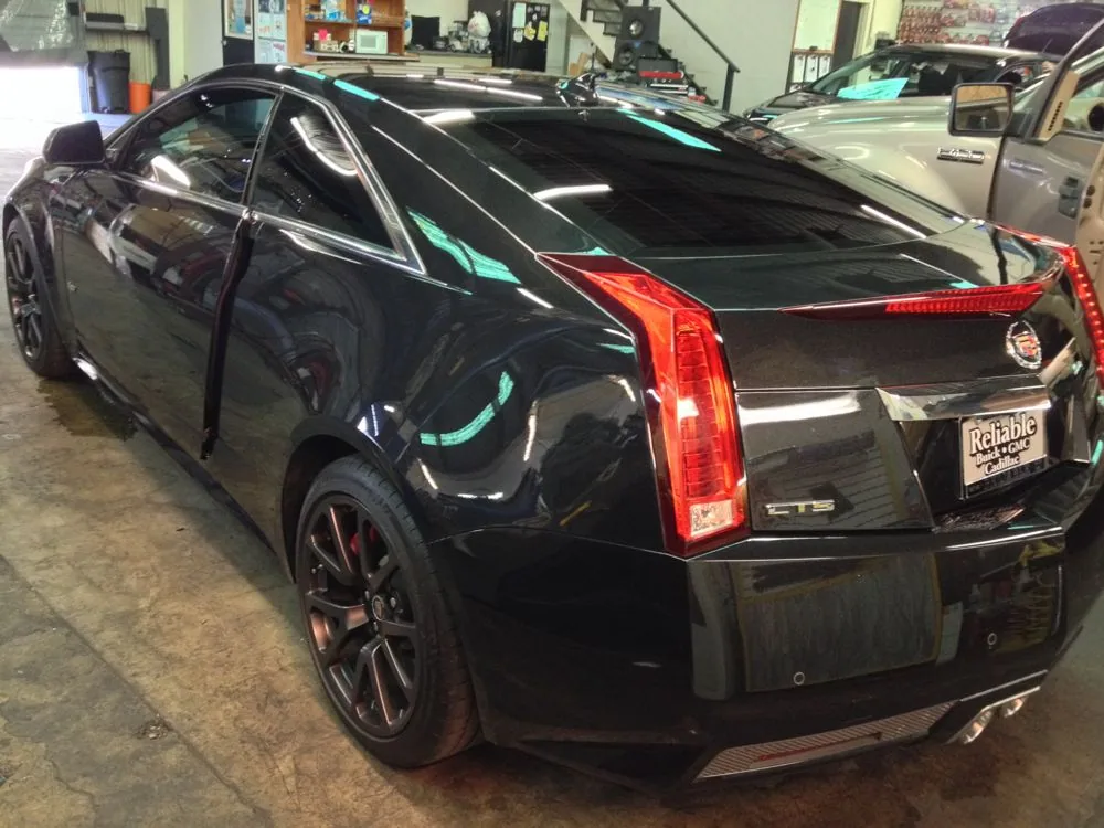 Black Cadillac CTS coupe with red brake lights parked in auto shop with open driver door