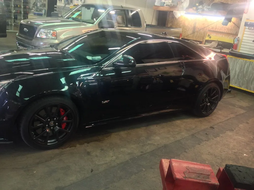 Black sports coupe with dark tinted windows and red brake calipers parked in an auto shop garage